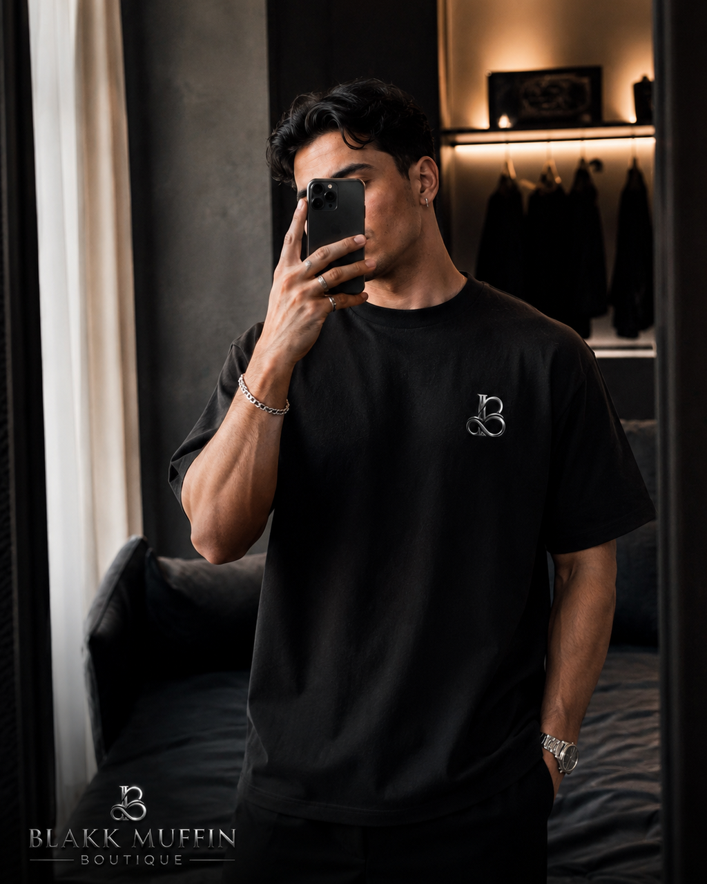 Man taking a mirror selfie wearing a black t-shirt with a logo in a room.